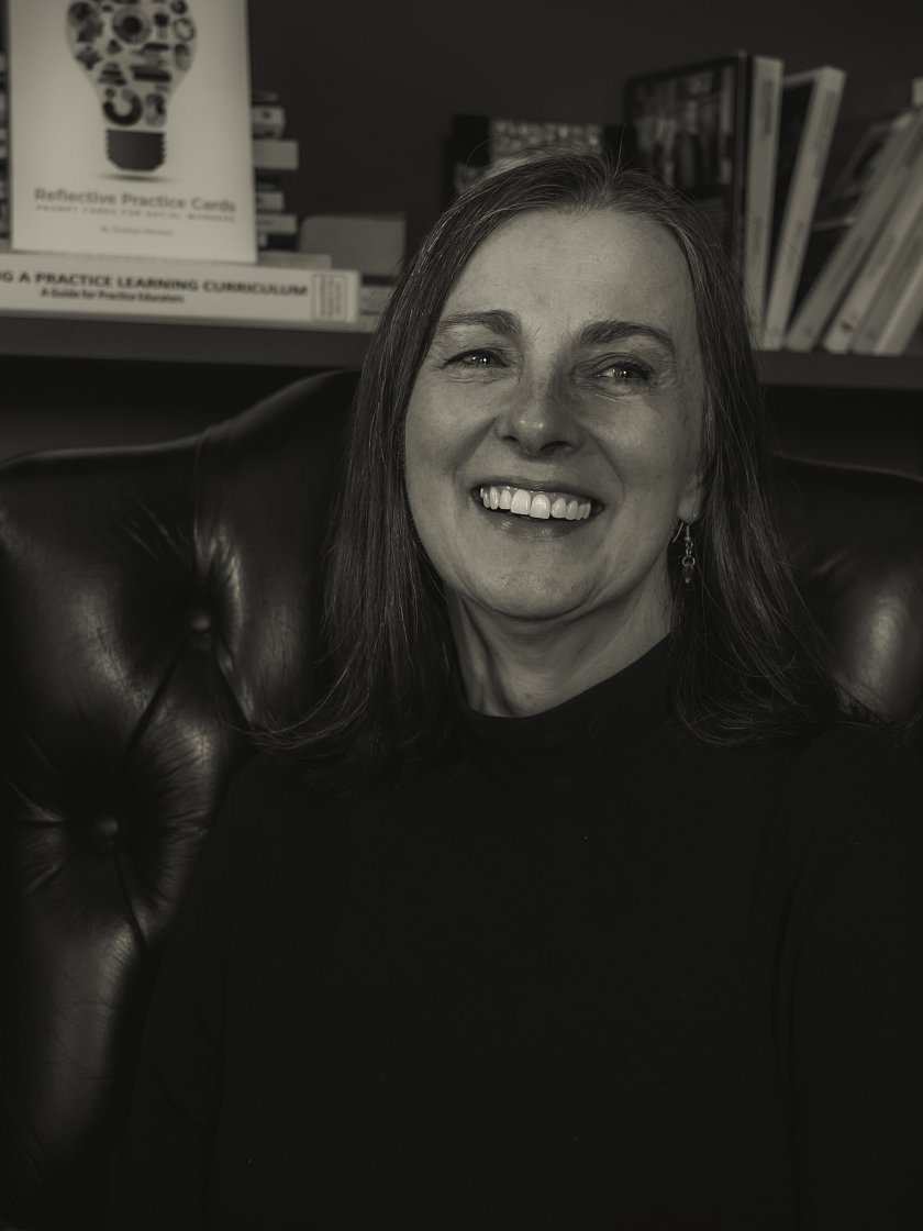 A photo of Siobhan stylised in black and white. On a shelf behind her are Reflective Practice Cards, Developing a Practice Learning Curriculum and a number of other books.